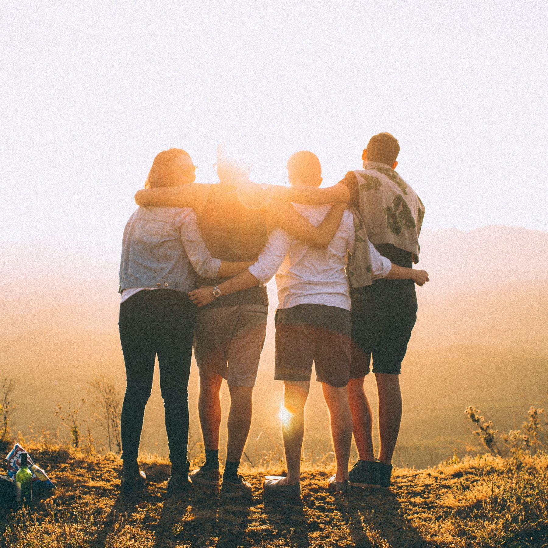 Friends standing together on a hill facing a bright sunset
